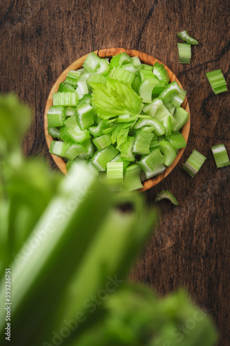 Green celery chopped pieces in bowl, wooden table, top view, copy space photo