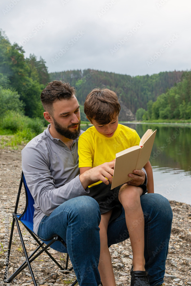 Family holiday and togetherness. Cute boy and her father are reading book in summer day