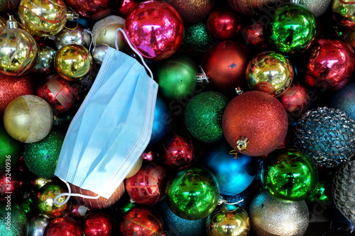 Top view of a pile of dark and colorful Christmas balls with a surgical face mask for holiday celebration during covid-19 pandemic concept. 