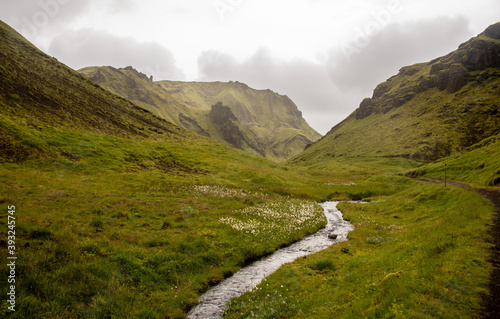 Fotografia Narrow stream surrounded by rocky hills covered in greenery under a cloudy sky