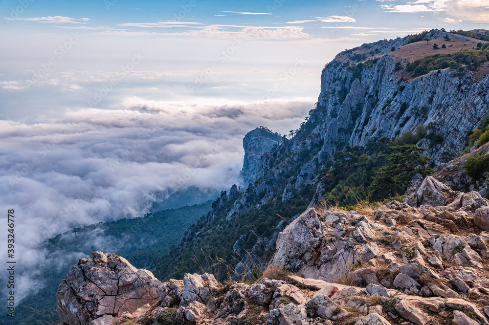 Obraz premium A majestic view of the rocky mountains and the valley in fog and clouds. Creamy fog covered the mountain valley in sunset light. Picturesque and gorgeous scene. Misty sunset over Crimea Mountains