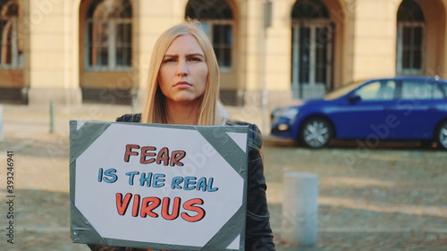 Blonde woman protesting that fear is the real virus on protest march. She holding banner in her hands and walking on the street. © art24pro
