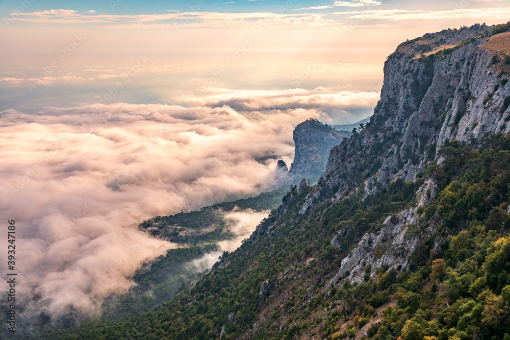 A majestic view of the rocky mountains and the valley in fog and clouds. Creamy fog covered the mountain valley in sunset light. Picturesque and gorgeous scene. Misty sunset over Crimea Mountains