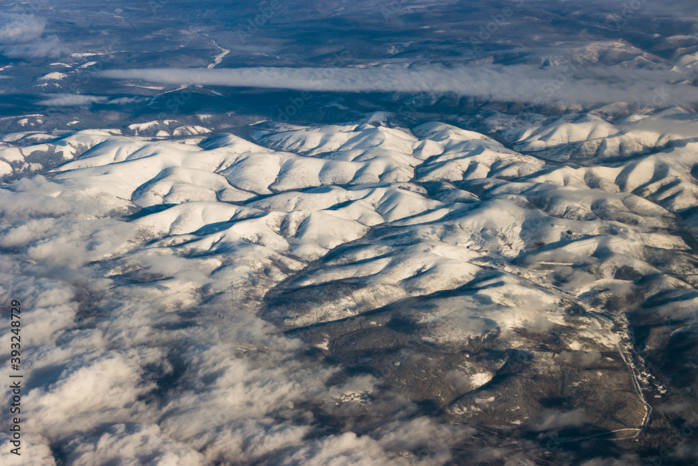 Fototapeta premium Snowy mountains from a bird's eye view on a clear blue sky with clouds.