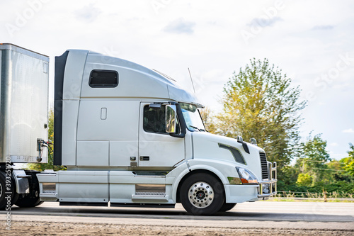 Big rig bonnet white long haul semi truck transporting cargo in dry van semi trailer driving on the highway road for timely delivery