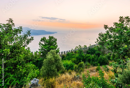 scenic view at picturesque sunset from high mountain with bushes and green trees below and beautiful cloudy sky, sea with far coast, sun glow with reflection on the background , castle landscape © Yaroslav