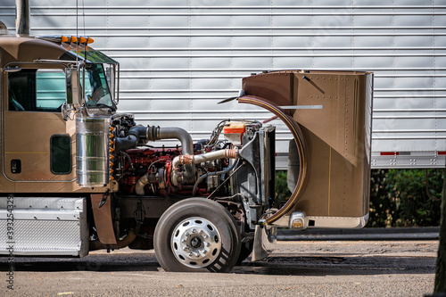 Brown big rig semi truck with open hood for checking that the engine is working properly during a stop in the delivery schedule