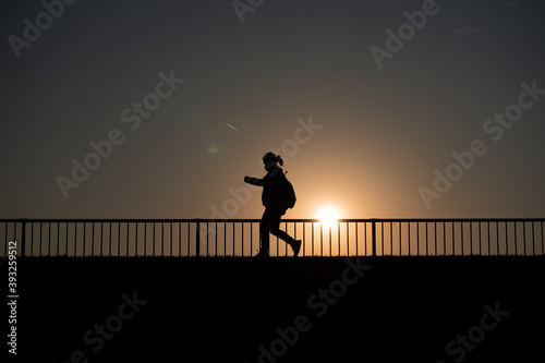 新型コロナウイルスの中、一人ウォーキングで健康維持する女性・夕日を背景にシルエット © 大出正一