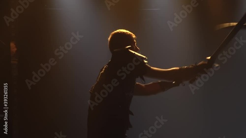 Men fight with swords in a dark studio with stage lighting. Silhouettes of male actors in armor performing in a theatrical show. Close up in slow motion.