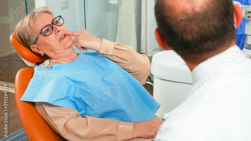Close up of elderly woman complaining to stomatologist about painful feelings in teeth. Senior patient explaining dental problem to dentistry doctor indicating mouth while examining radiography.