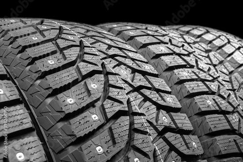 Winter studded tire. Winter car tires isolated on black background. Tire stack background. Tyre protector close up. Square powerful spikes. Black studdable winter tyre profile. Car tires in a row
