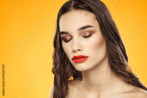Beautiful brunette naked shoulders bright makeup red lips hairstyle close-up yellow background