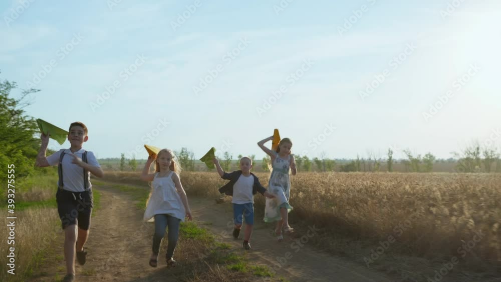 group of friends, boys and girls running along a dusty country road and launch paper planes into the air near the golden wheat field group of friends, boys and girls running along a dusty country road and launch paper planes into the air near the golden wheat field