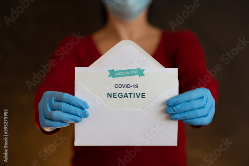 Woman Holding Negative Antigen Detection Test for Covid-19. Person Wearing Face Mask and Blue Surgical Gloves Showing Open Envelope with Negative Result in Rapid Medical Test into Camera.