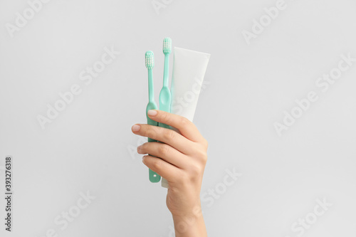 Female hand with toothbrushes and paste on light background