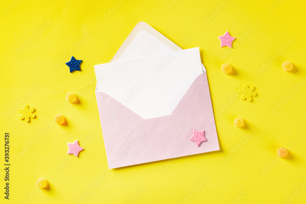 A greeting card in a pink envelope, shot from above on a yellow background glitter stars and candies