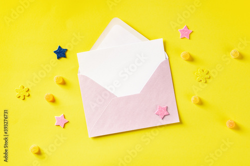 A greeting card in a pink envelope, shot from above on a yellow background glitter stars and candies