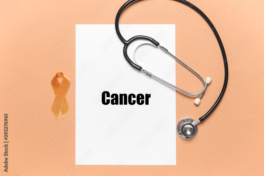 Paper sheet with word CANCER, stethoscope and golden ribbon on color background Paper sheet with word CANCER, stethoscope and golden ribbon on color background