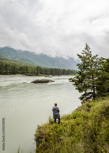 Woman admiring the rapid flow of a mountain river on the background of mountains covered with clouds