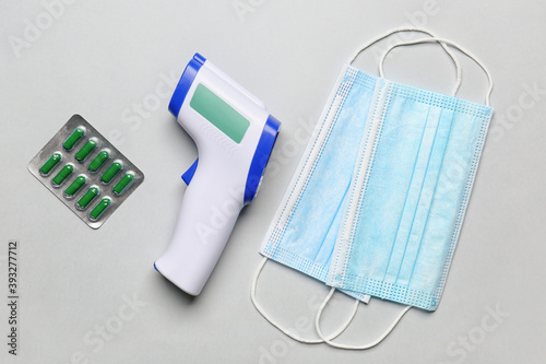 Infrared thermometer, masks and pills on light background
