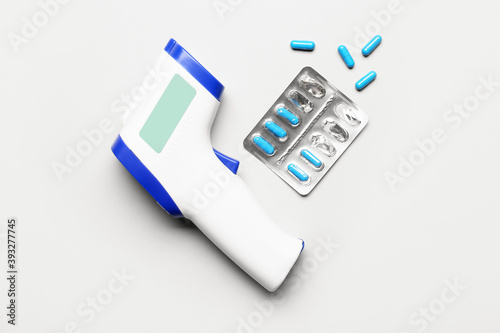Infrared thermometer and pills on light background