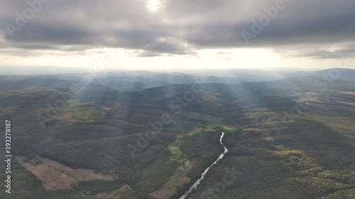 Sun rays over forest fields with a river
