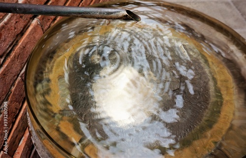 A drop of clear water dripping into a golden metal basin, a diffusion of water droplets in the hot summer sun