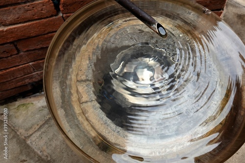 A drop of clear water dripping into a golden metal basin, a diffusion of water droplets in the hot summer sun