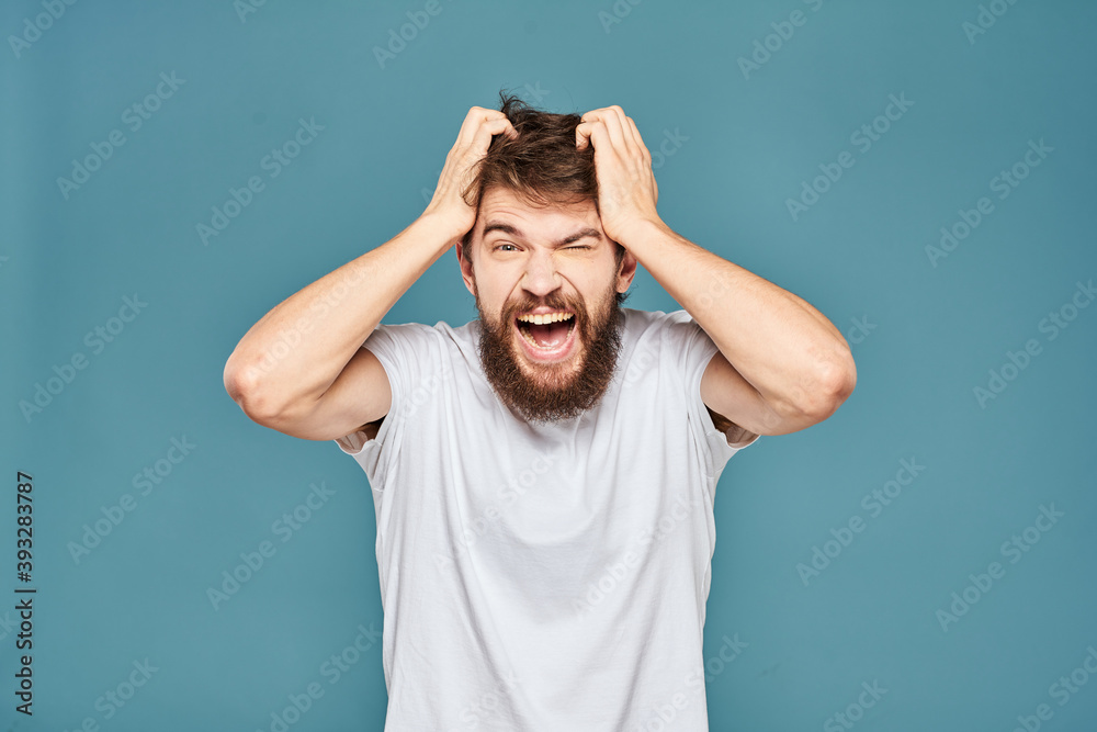 A bearded man in a white T-shirt gestures with his hands emotions blue background A bearded man in a white T-shirt gestures with his hands emotions blue background