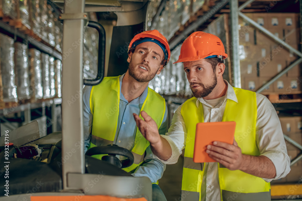Warehouse worker showing something to his colleague Warehouse worker showing something to his colleague
