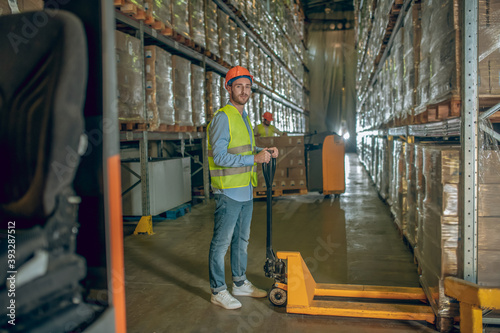 Worker in a vest and helmet standing in the warehouse in the aisle