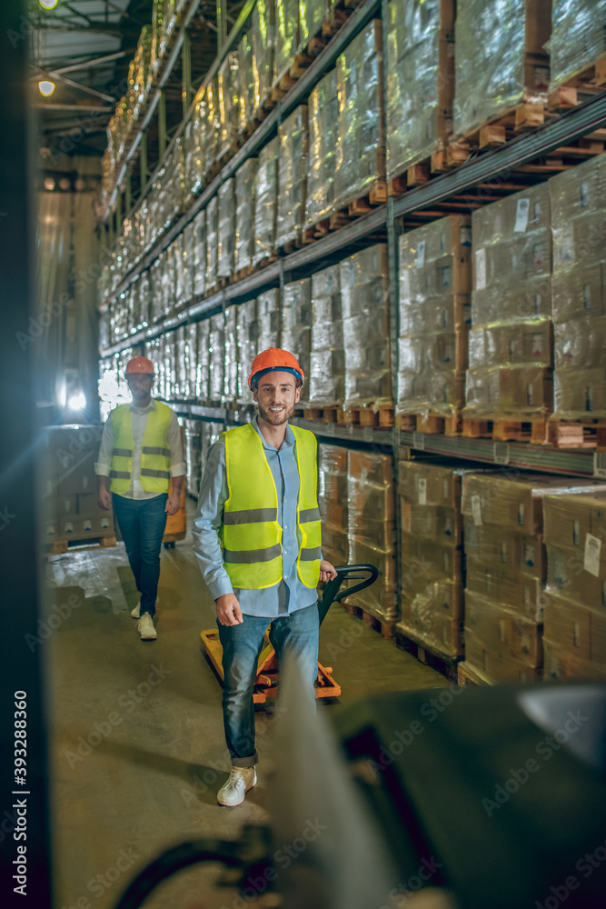 Worker in a yellow vest and helmet standing near the shelves with boxes Worker in a yellow vest and helmet standing near the shelves with boxes