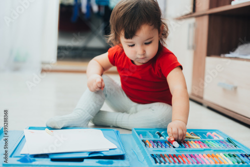 A little girl in a red t-shirt is drawing with a red marker on a blue easel