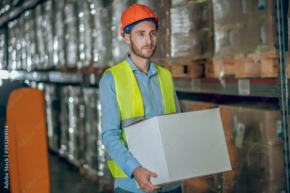Young male worker carrying a box and looking serious Young male worker carrying a box and looking serious