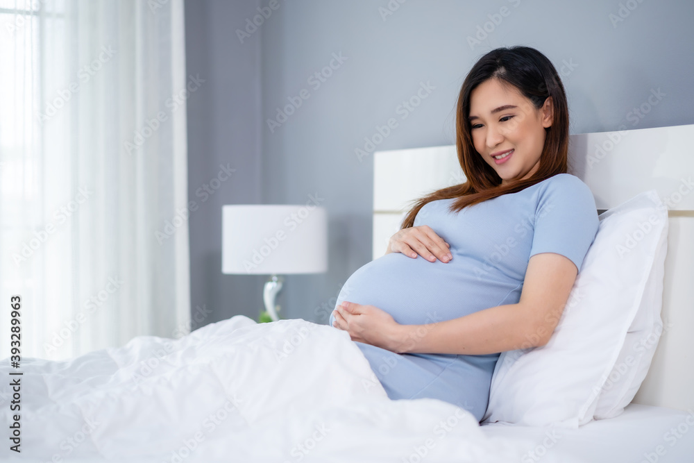 happy pregnant woman stroking her belly on bed happy pregnant woman stroking her belly on bed