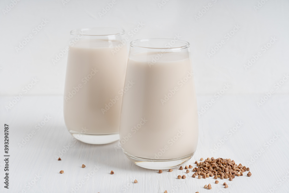 Gluten-free and lactose-free healthy buckwheat milk full of vitamins, minerals and antioxidants served in two tall drinking glasses with raw grain ingredient on white wooden background. Horizontal Gluten-free and lactose-free healthy buckwheat milk full of vitamins, minerals and antioxidants served in two tall drinking glasses with raw grain ingredient on white wooden background. Horizontal