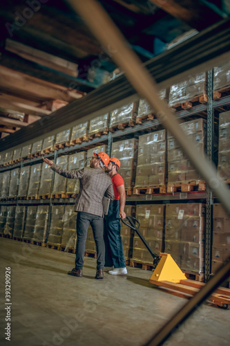 Manager talking to a warehouse worker and showing him containers on the shelves