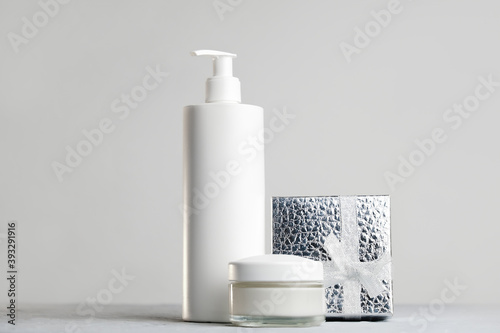 Blank cosmetics bottles with silver gift box on grey background. Cosmetics container and cream jar mockup, Christmas concept.