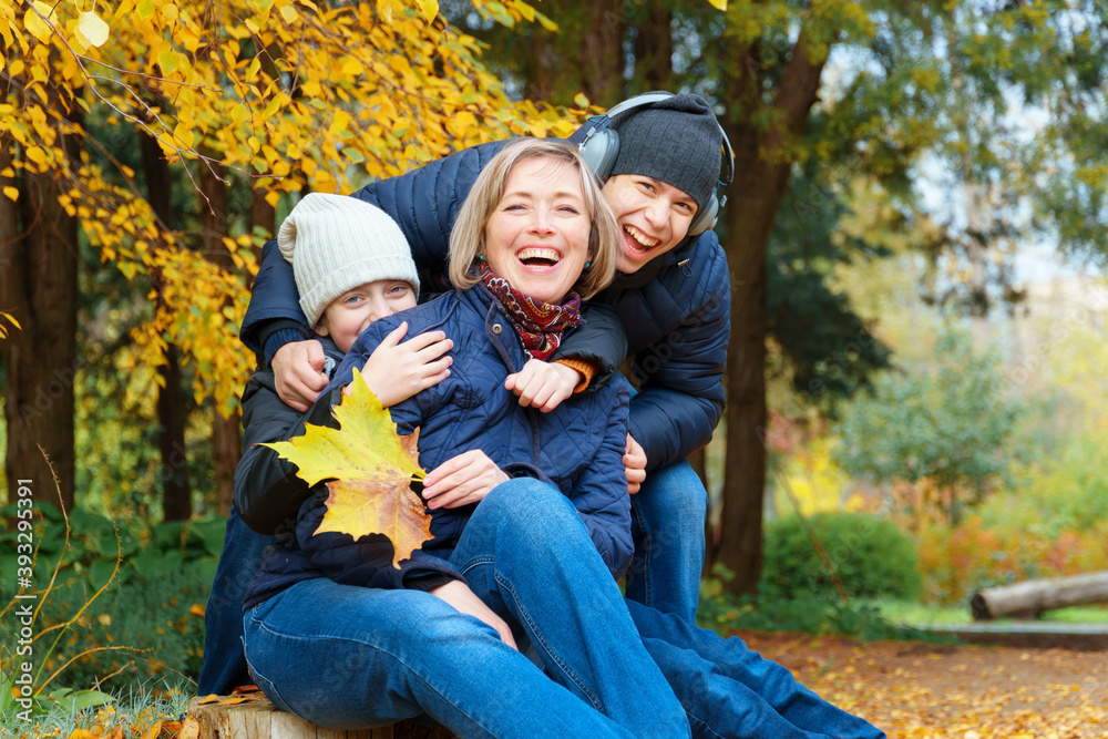 Fototapeta premium portrait of a mother and son and daughter in autumn city park, happy people together, parent and children talking and smiling, sitting on a stump, beautiful nature