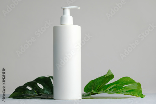 Blank plastic cosmetics container for cream or shampoo. Cosmetics bottle mockup with tropical leaves. Beauty product design, skincare and haircare concept.