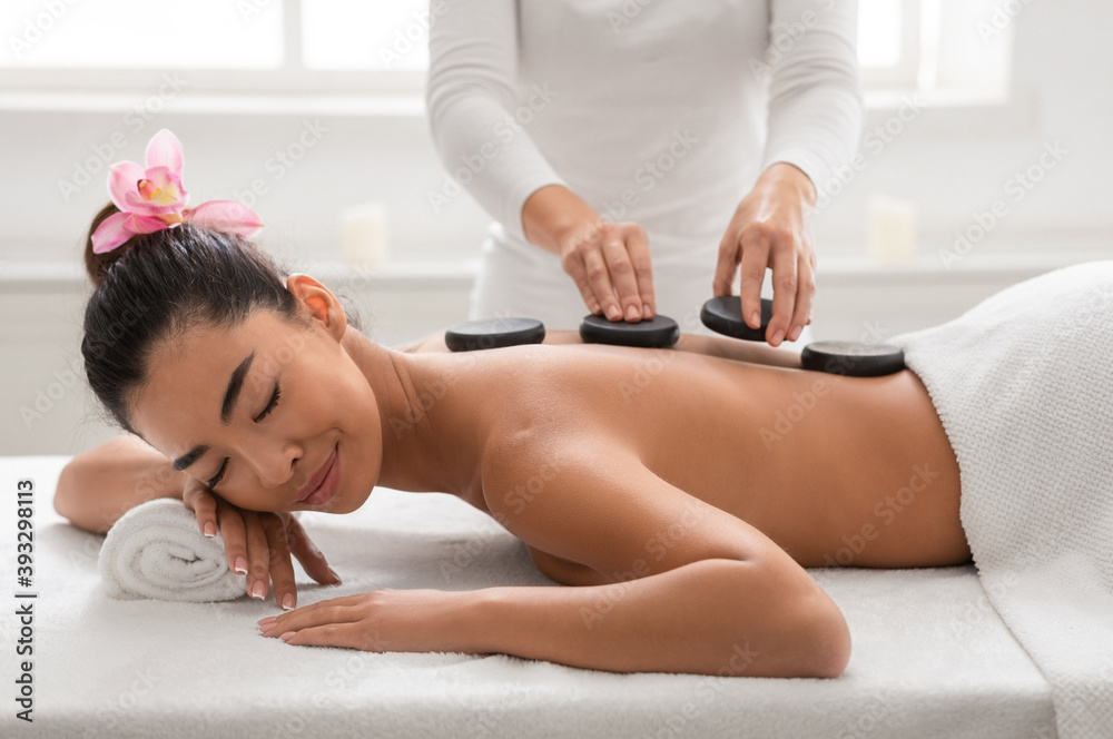 Relaxed asian woman enjoying hot stones back massage in spa salon