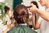 Makeup artist and hairdresser are preparing hairstyle and visage of young woman in beauty salon