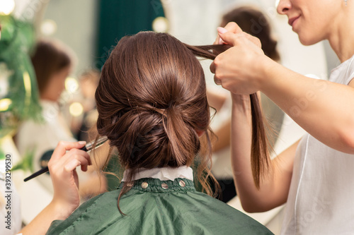 Makeup artist and hairdresser are preparing hairstyle and visage of young woman in beauty salon