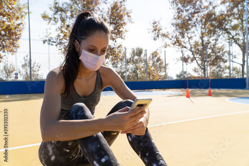Young lady in a court using her phone wearing a sanitary mask - concept of the new normal photo
