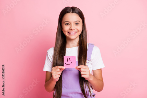 Photo of pretty kid girl hold sticker with smiling emoticon isolated over pink pastel color background