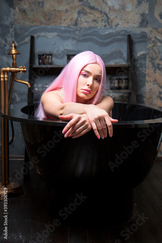 female with long pink hairs is lying in the black bath in dark luxury bathroom