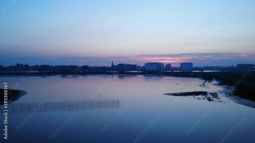 Dutch nature and cities combined in one pedestal and dolly drone shot. Barge sailing on a river while the sun is rising on a foggy landscape behind buildings Dutch nature and cities combined in one pedestal and dolly drone shot. Barge sailing on a river while the sun is rising on a foggy landscape behind buildings