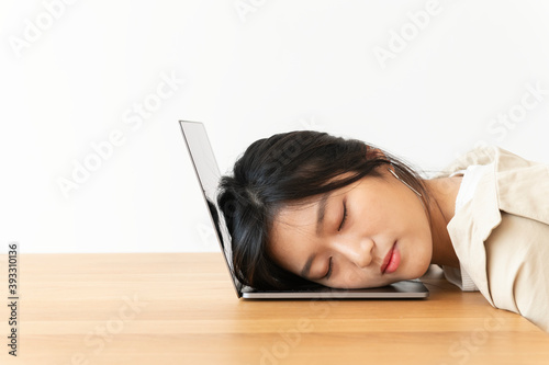 Tired Asian woman resting her head on a laptop