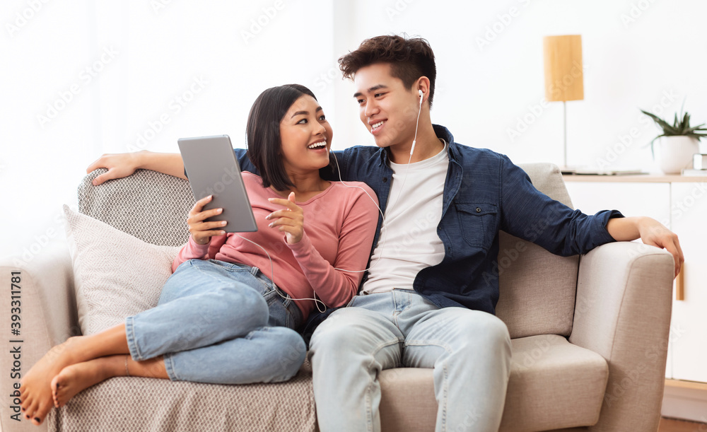 Japanese Spouses Using Tablet Browsing Internet Sitting On Couch Indoor