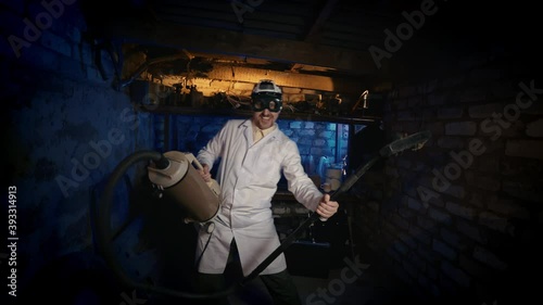 A nutty professor with an old vacuum cleaner is dancing in an old garage. Computer nerd with a mustache and wacky glasses.
